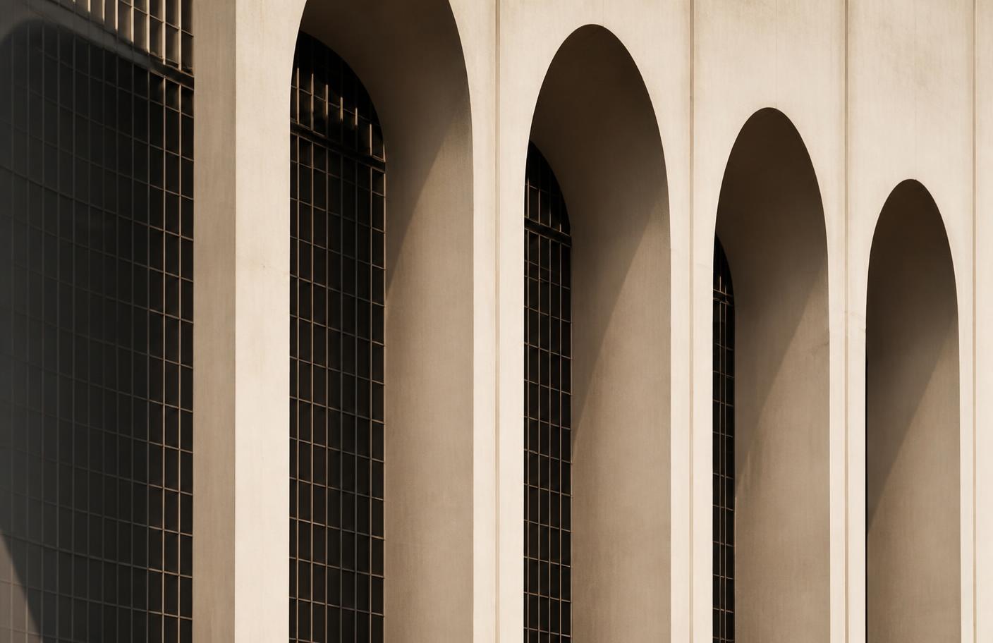 Concrete arches and steel window grids in warm ivory light with strong geometric shadows